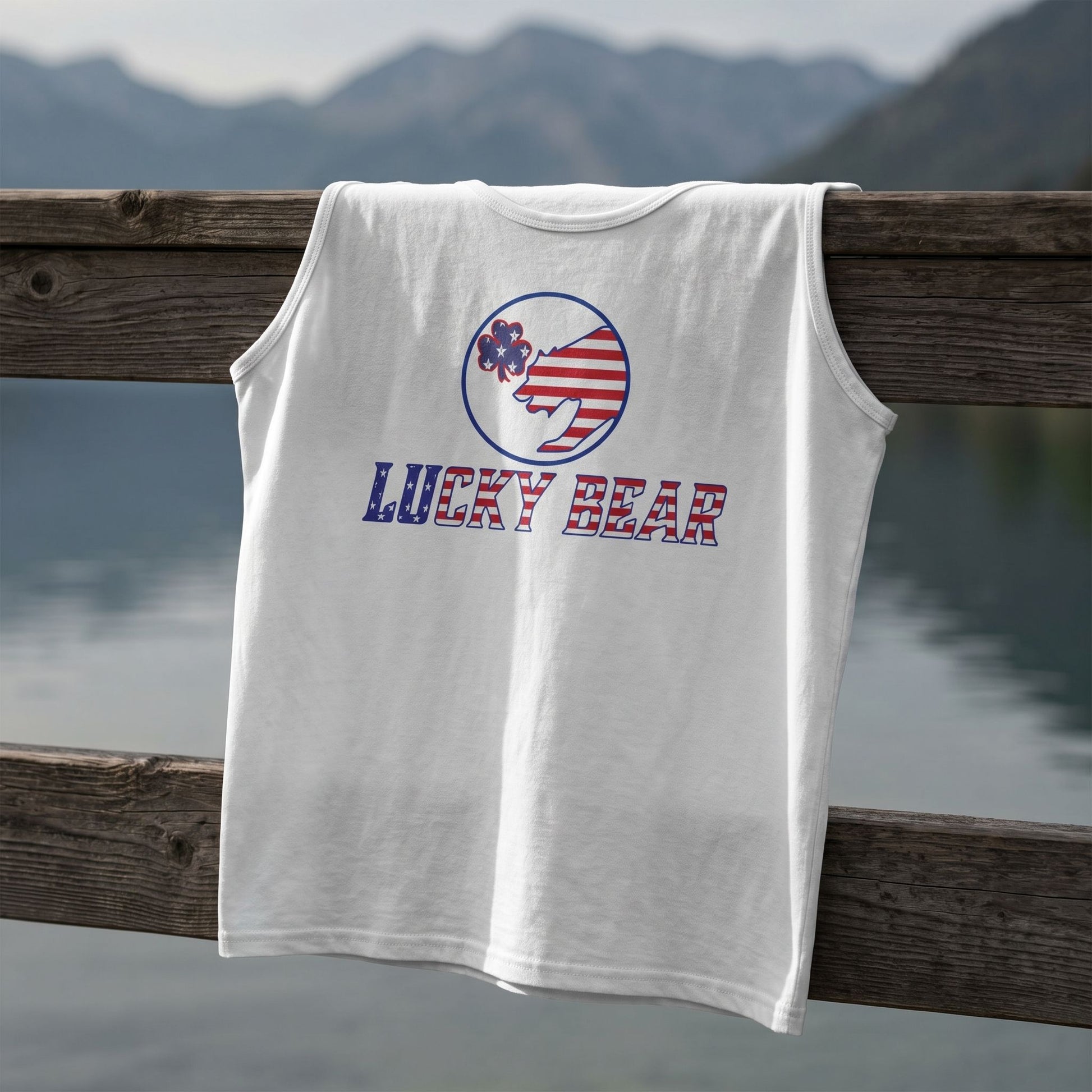Close-up of All American Luck men's tank top on a dock railing by a mountain lake, highlighting fabric texture, stitching, and cotton quality.