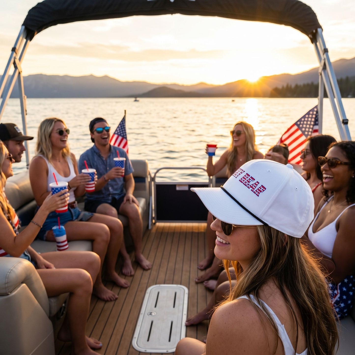 Small All-American Rope Cap on boat deck with Lake Tahoe sunset, showing embroidered flag and relaxed outdoor celebration scene.