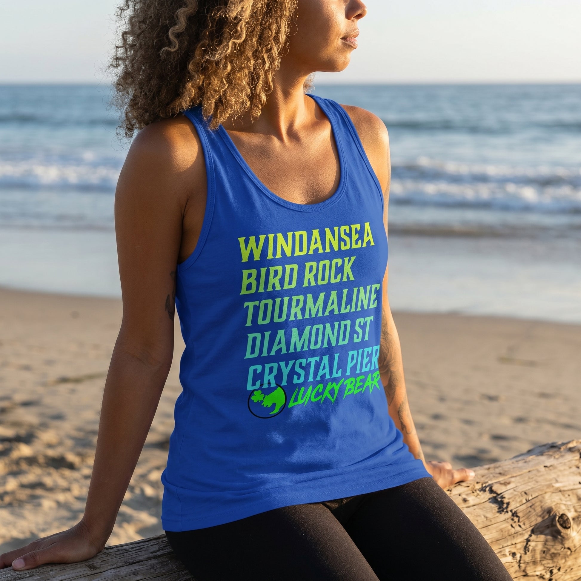 Model seated on a beach during golden hour wearing Lucky Breaks Tank Top, showcasing relaxed fit and fabric texture with warm sunlight.