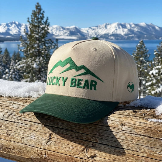 Close-up of green Sierra 5 panel cap on wood with snow-covered mountains in winter background.
