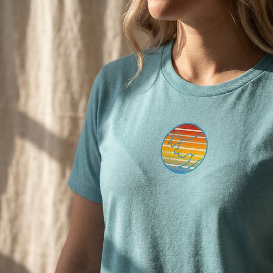 Close-up of Women's Retro Sunset T-Shirt on linen backdrop, highlighting vintage sunset logo and fabric details in natural afternoon light.