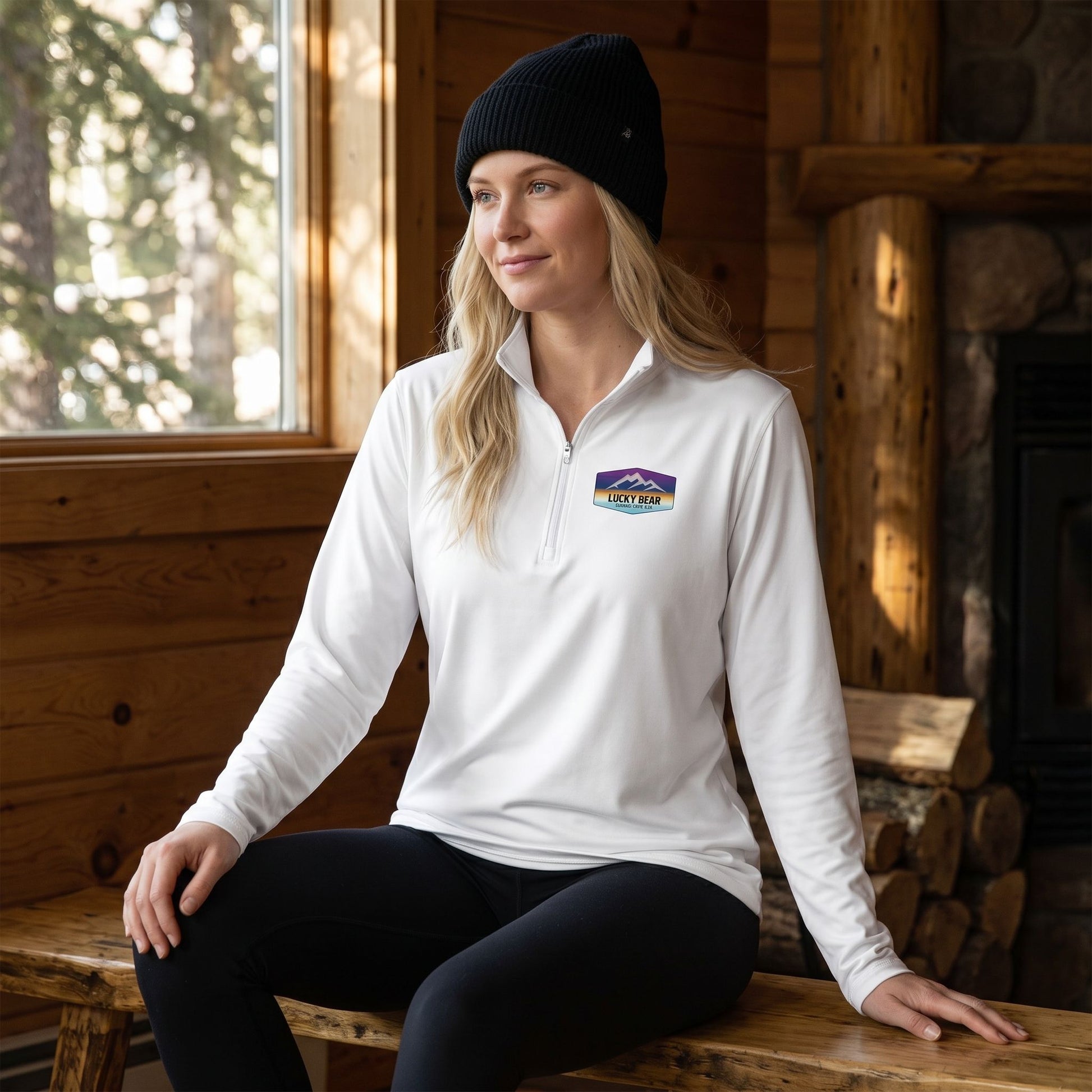 Blonde female model in white Sierra Sunset pullover with leggings and black beanie in cozy mountain cabin setting.