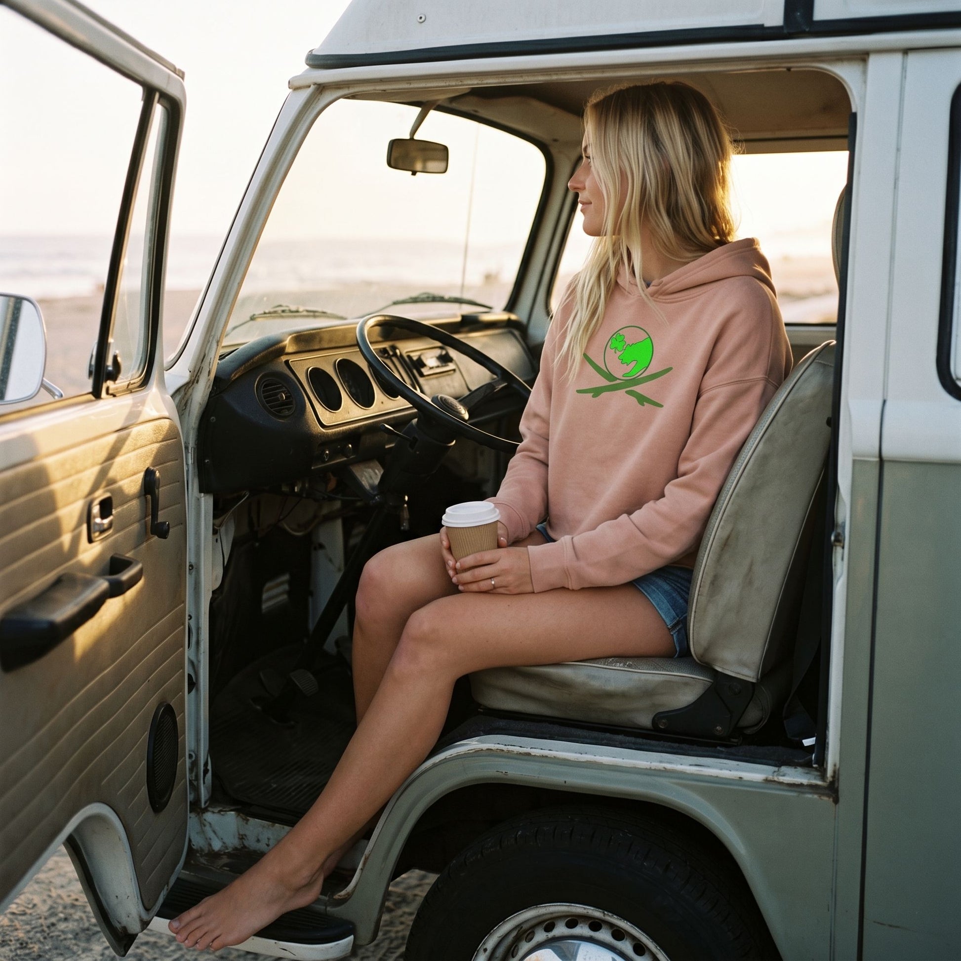Blonde female sitting in a vintage Volkswagen van wearing a pink Surf Club Logo Crop Hoodie, holding coffee and showcasing comfort and style.