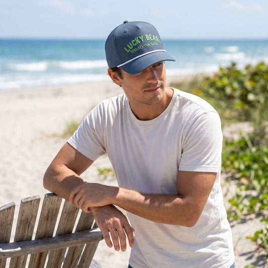 Full-body of a model outdoors on a beach wearing the Spread the Luck rope cap tilted back to show its mid-profile fit against a sunny beach scene.