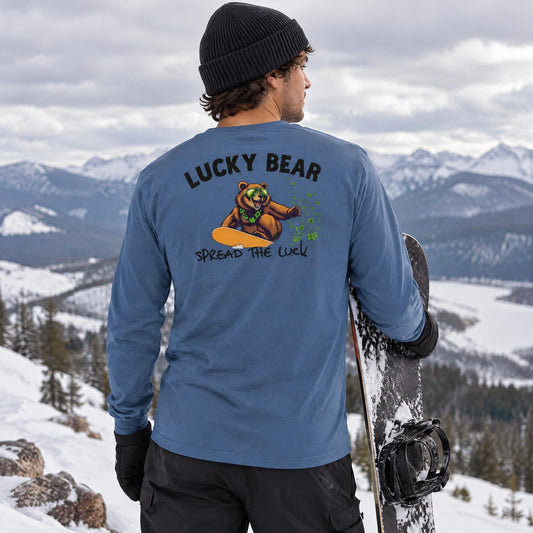 Model wearing an indigo blue long sleeve shirt with a bear snowboarding graphic on the back, standing on a mountain top.