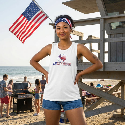 Woman in Ladies’ All American Luck Muscle Tank at beach BBQ with blue shorts and American flag accessories.