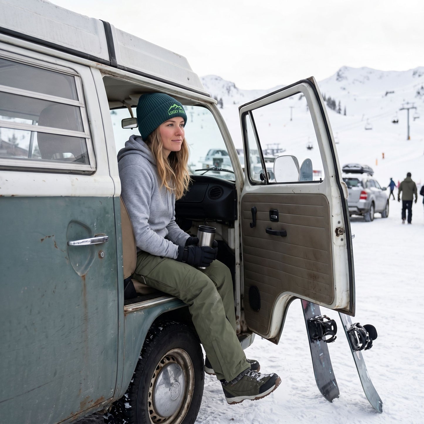 Model wearing the Sierra Summit Fisherman beanie sitting in a vintage van at a snowy mountain resort, holding coffee, with snowboards nearby.