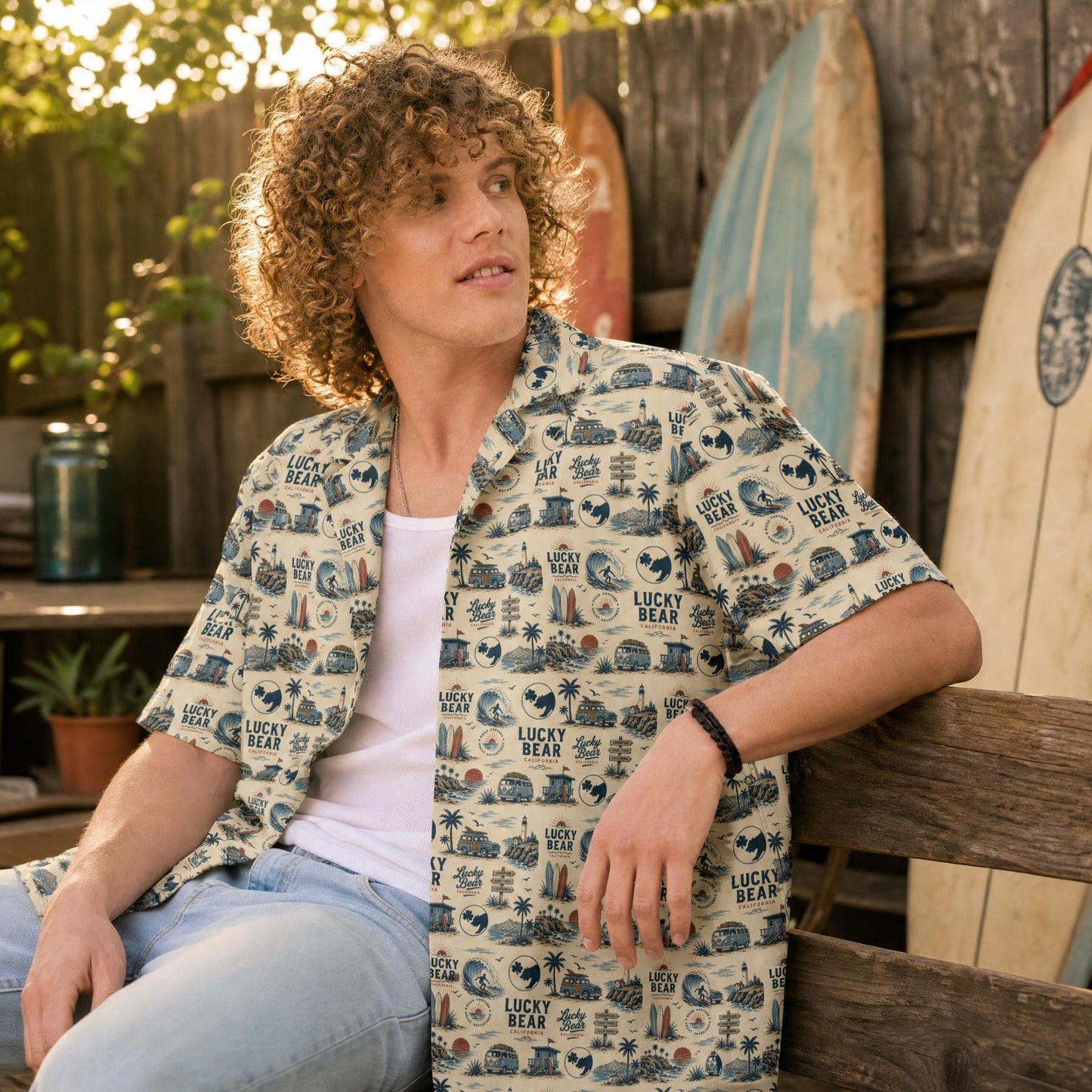 Blonde male model in Lucky Bear Americana Button-Up shirt in a cozy backyard with vintage surfboards and rustic fence, showcasing relaxed summer style.