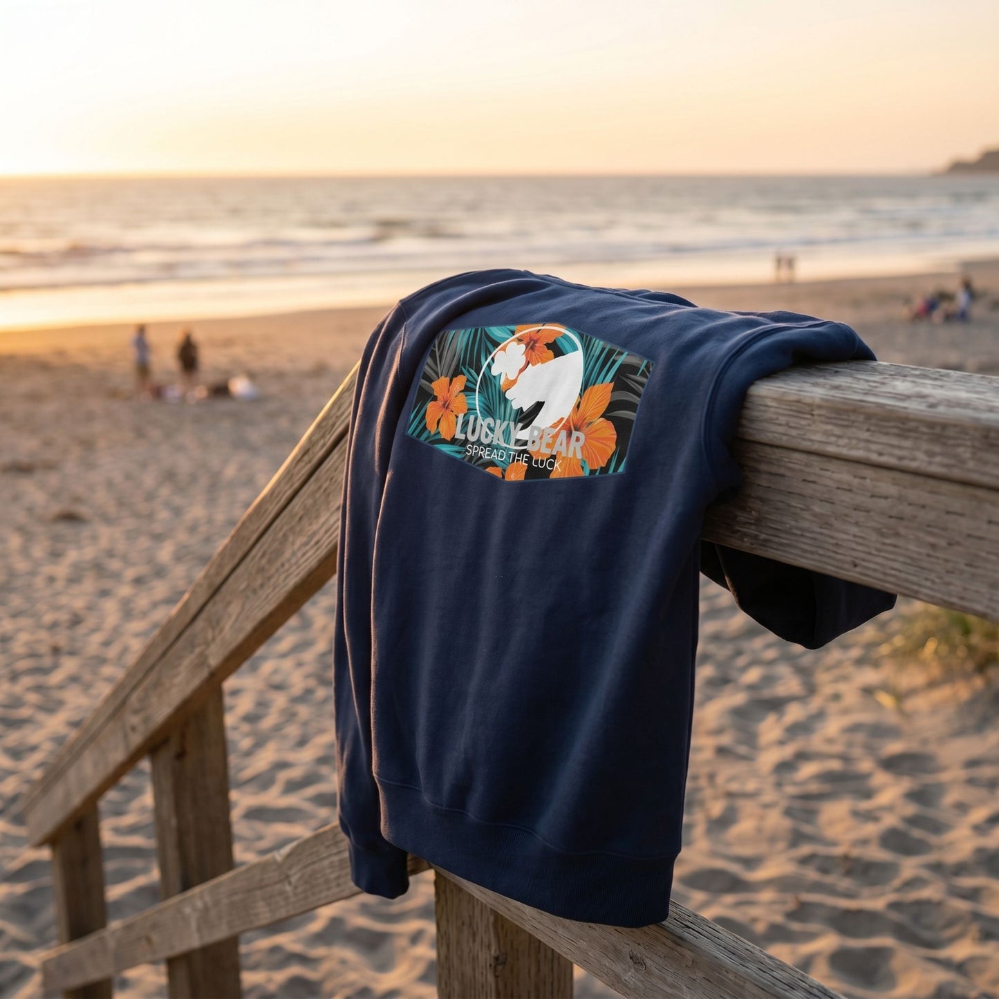 Close-up of Lucky Bear Tropical Zip Up Hoodie draped over a lifeguard tower handrailing, highlighting plush fleece texture and signature graphics with beach background.