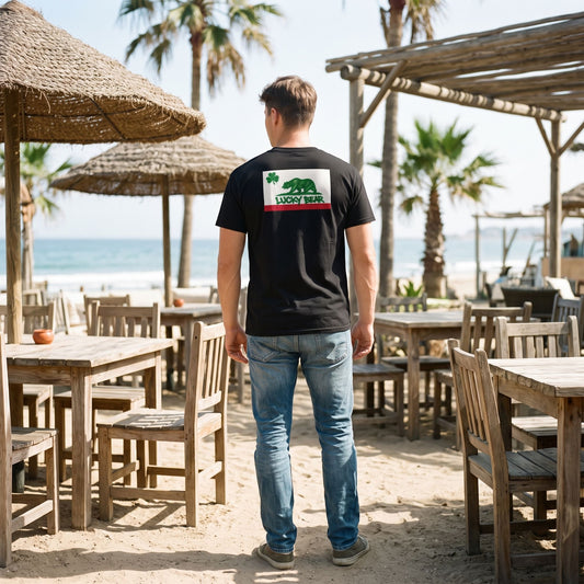 Model wearing a black cotton t-shirt with a California-inspired bear graphic at an outdoor beach cafe.