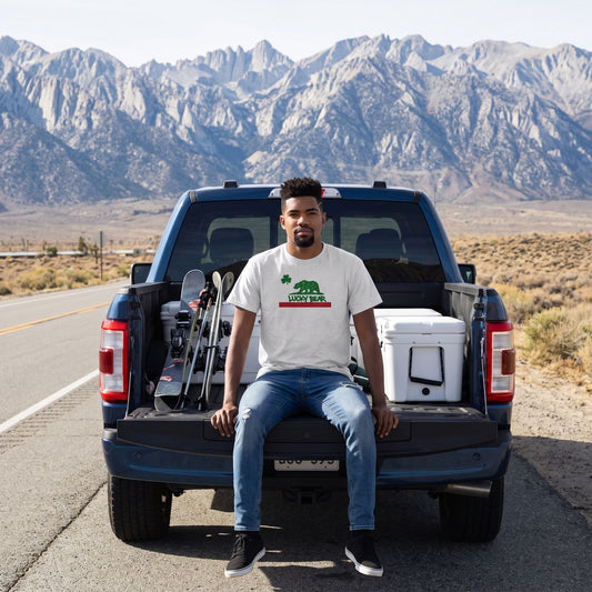 Male model wearing a grey Lucky Republic cotton t-shirt sitting on a truck tailgate with outdoor gear near the Sierra Nevada mountains.