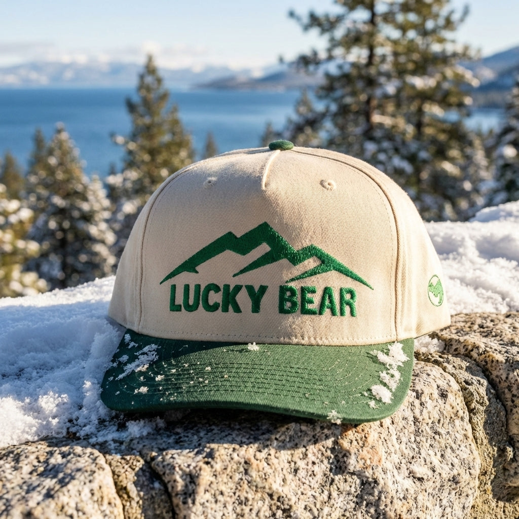 Close-up of green Sierra 5 panel cap on snow-covered stone with mountain scenery in background.