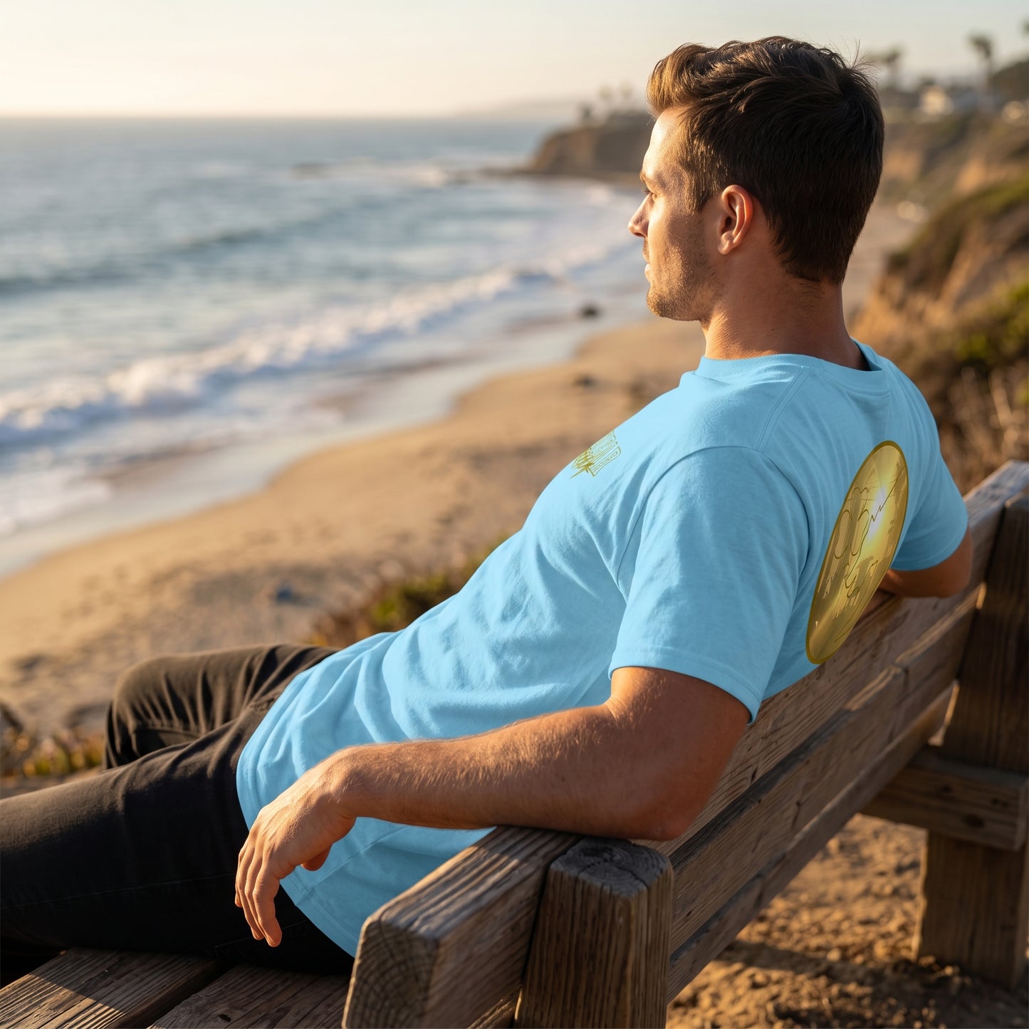 Male model lounging on beach bench wearing a white cotton sunset men's tee, focusing on side seam and sleeve with detailed fabric texture in warm golden hour light.