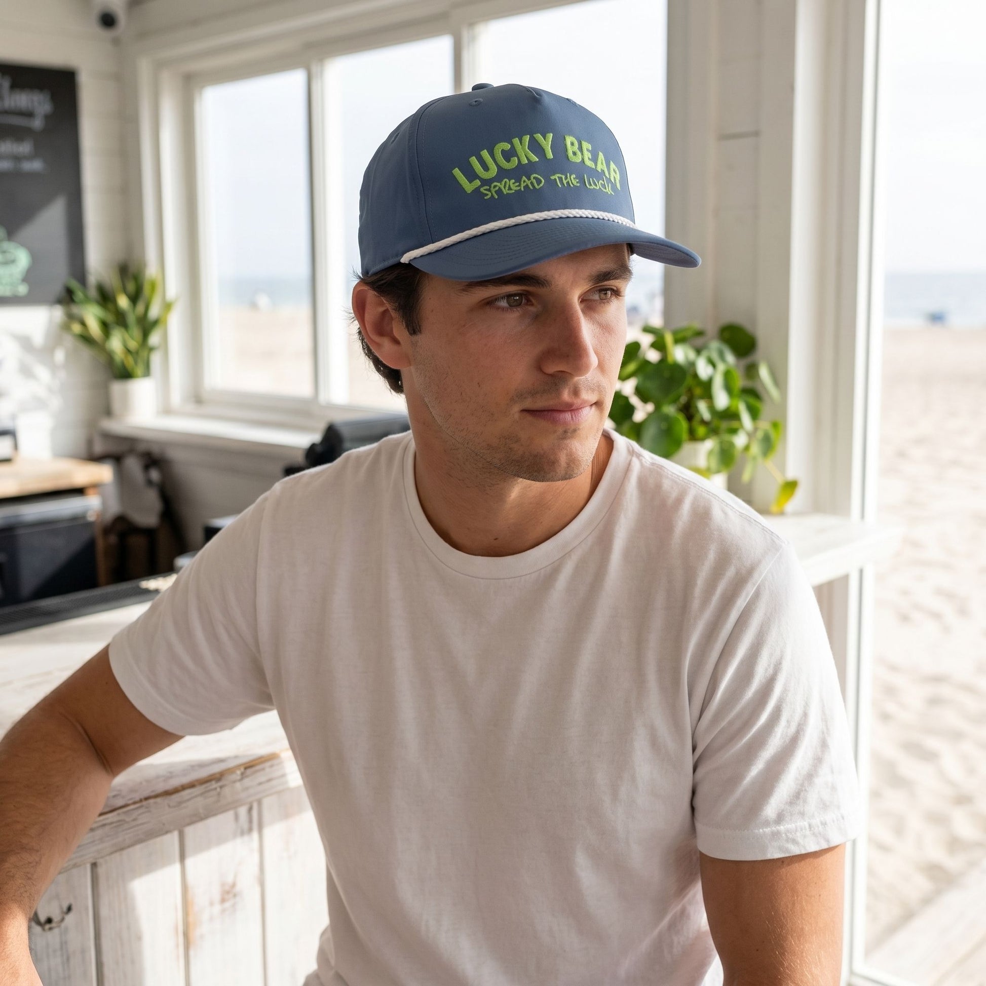 Close-up of a casually posed model at a beach cafe showing the classic silhouette and braided rope detail of the cap with soft natural lighting.