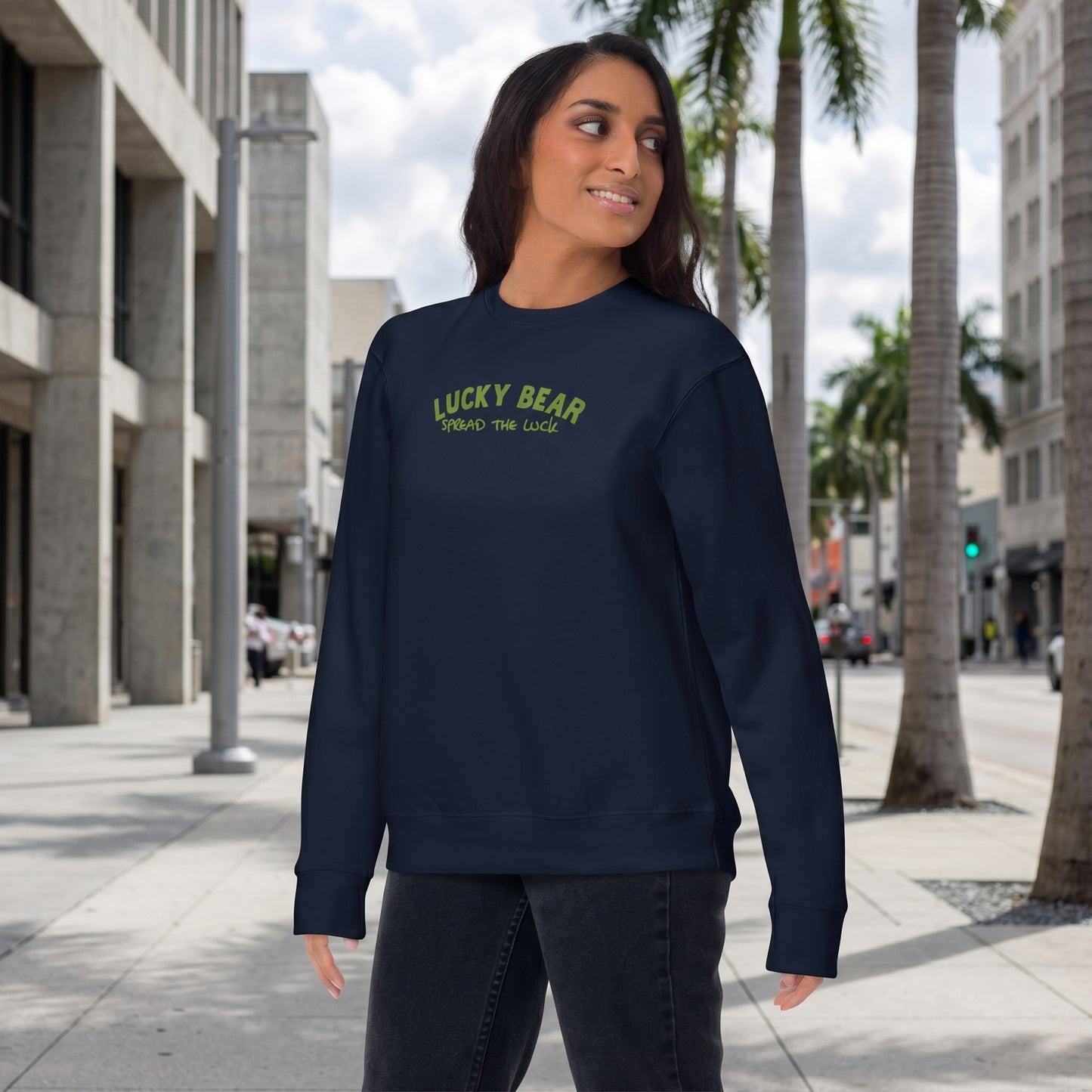 Full-body side view of model in navy Spread the Luck Sweatshirt on urban sidewalk with cityscape background.