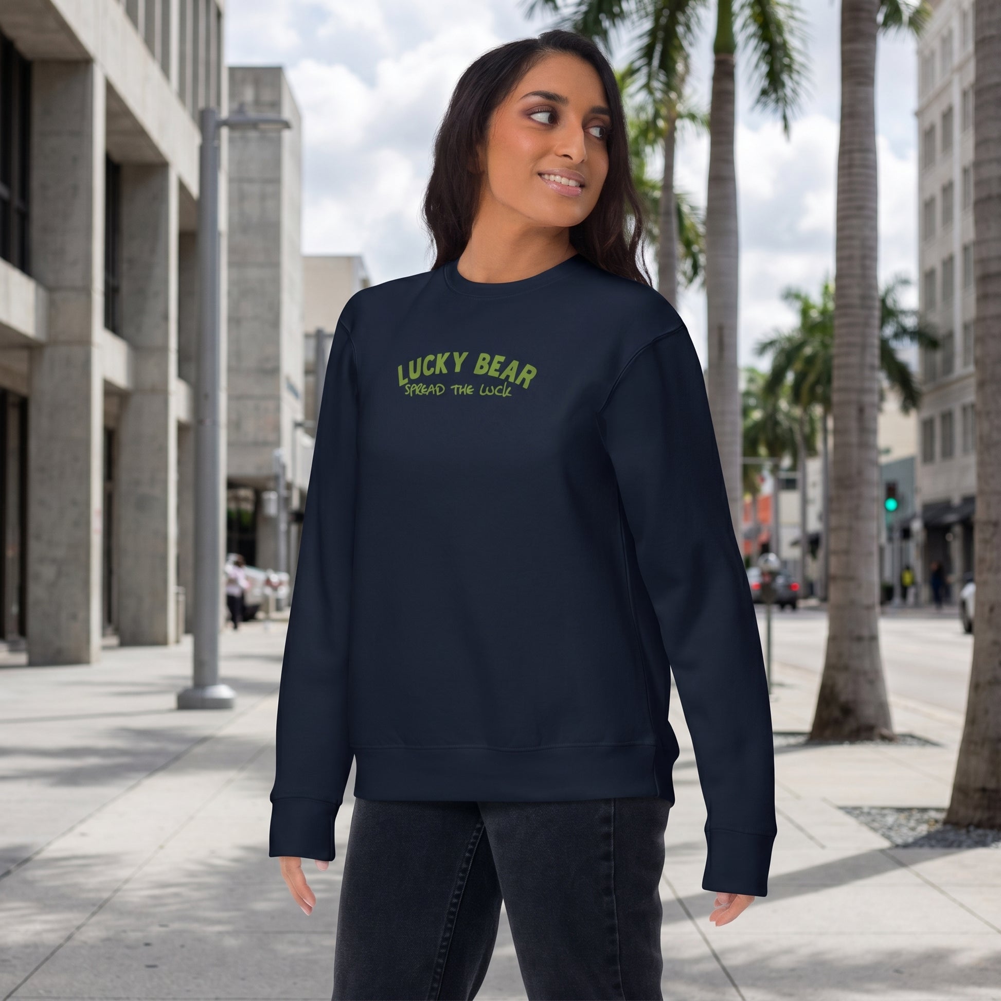 Full-body side view of model in navy Spread the Luck Sweatshirt on urban sidewalk with cityscape background.