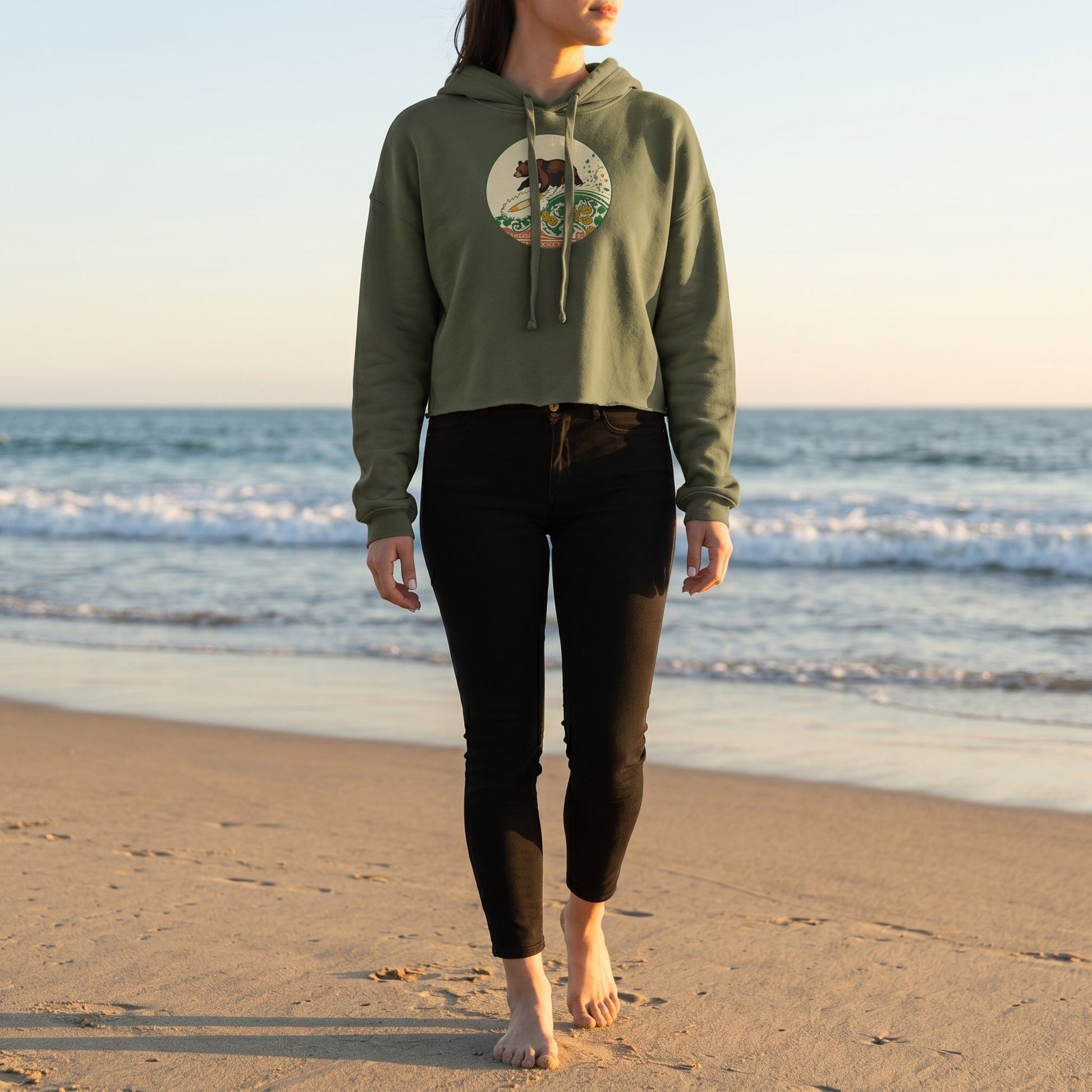 Full-body view of a model wearing the Surf Club Crop Hoodie outdoors on a sandy beach during golden hour.