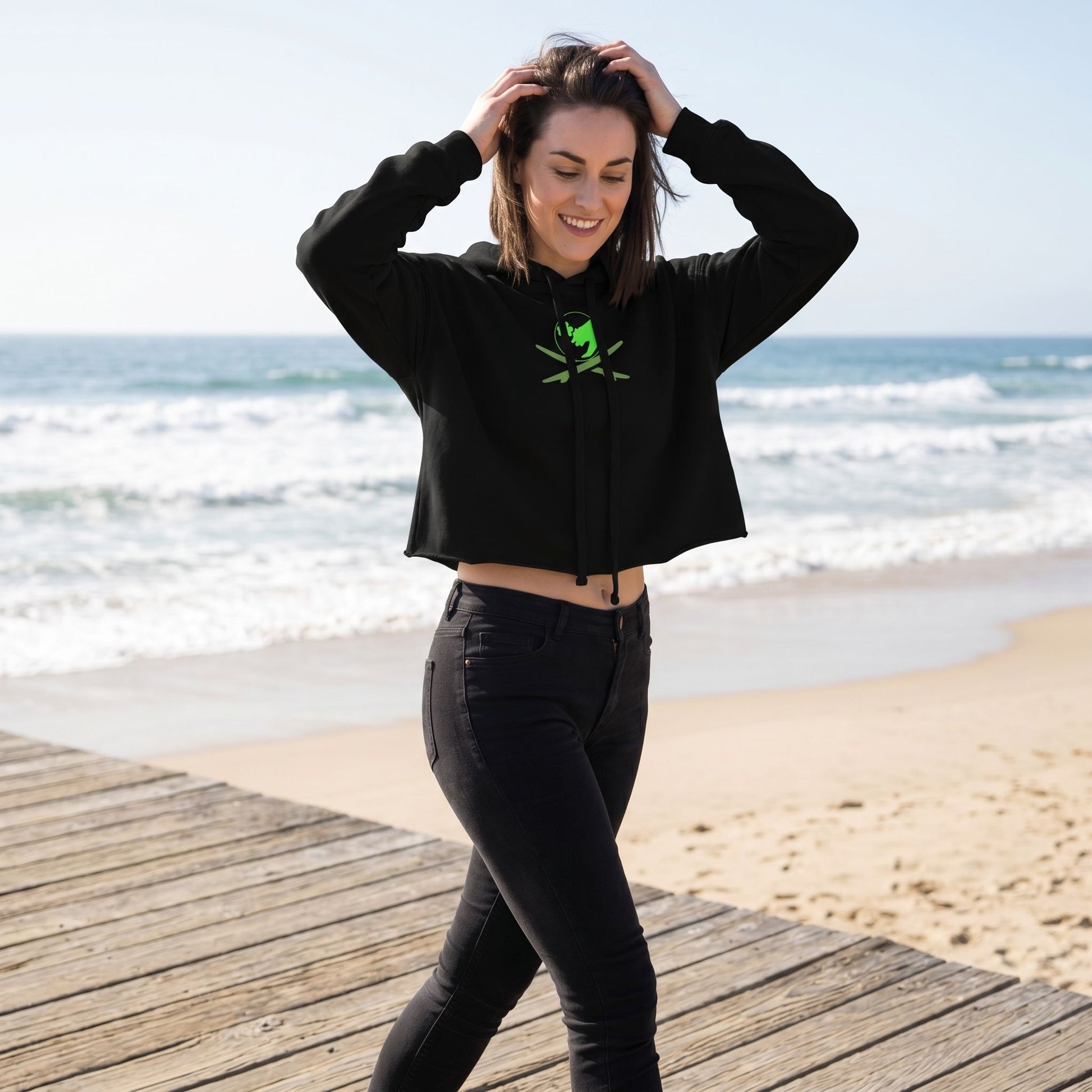 Model wearing Surf Club Logo Crop Hoodie outdoors on a sunny boardwalk near the ocean, highlighting relaxed fit and casual style.