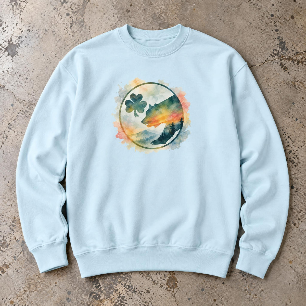 Mountain sunset sweatshirt with watercolor bear graphic laid flat on a textured concrete surface.
