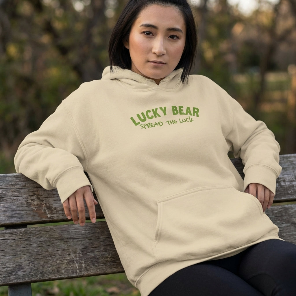 Model sitting outdoors in a natural scene, wearing the 'Spread the Luck' hoodie with visible texture, folds, and realistic fit.