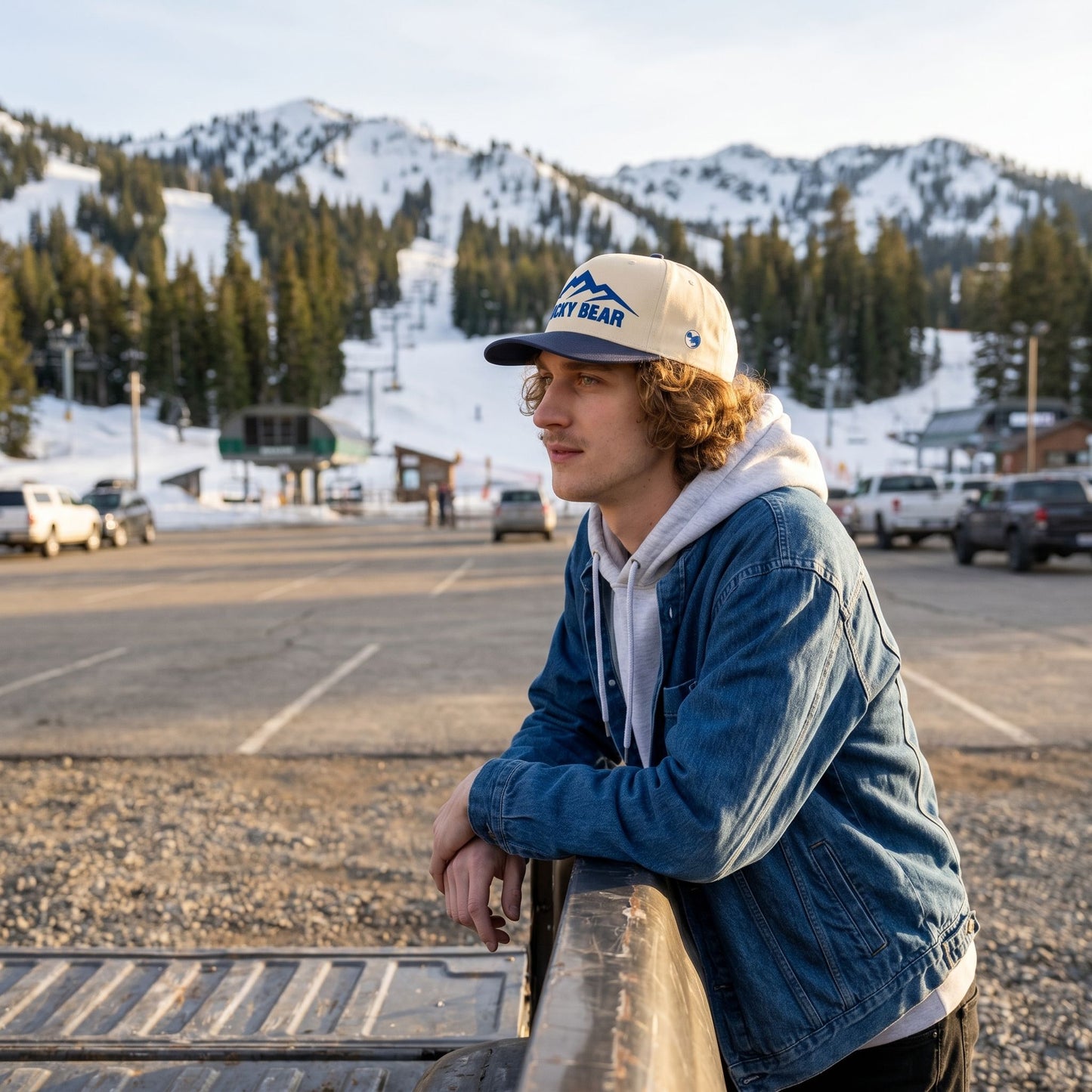 Full-body shot of blue Sierra 5 panel hat worn outdoors at ski resort, mountain background and golden hour lighting.