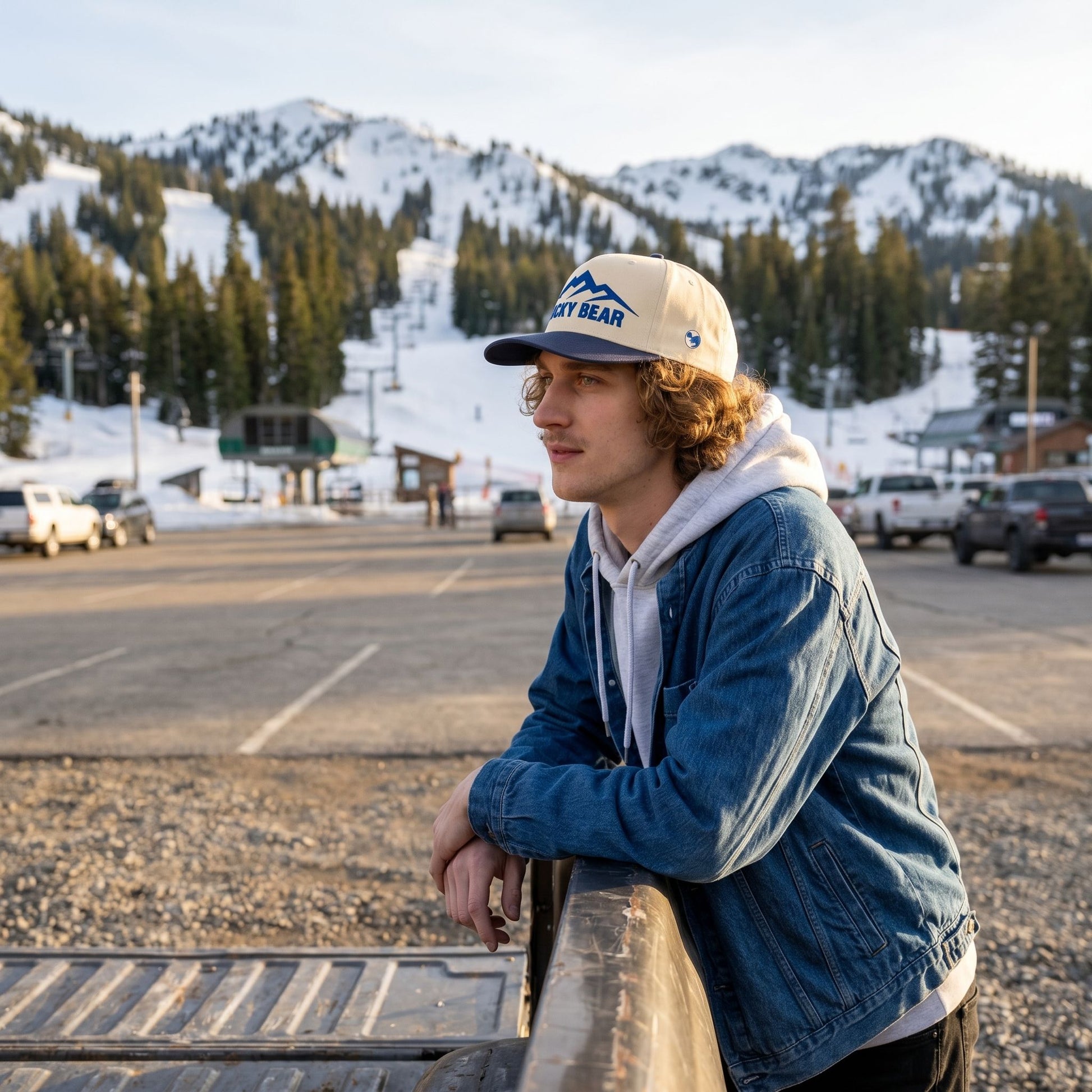 Full-body shot of blue Sierra 5 panel hat worn outdoors at ski resort, mountain background and golden hour lighting.