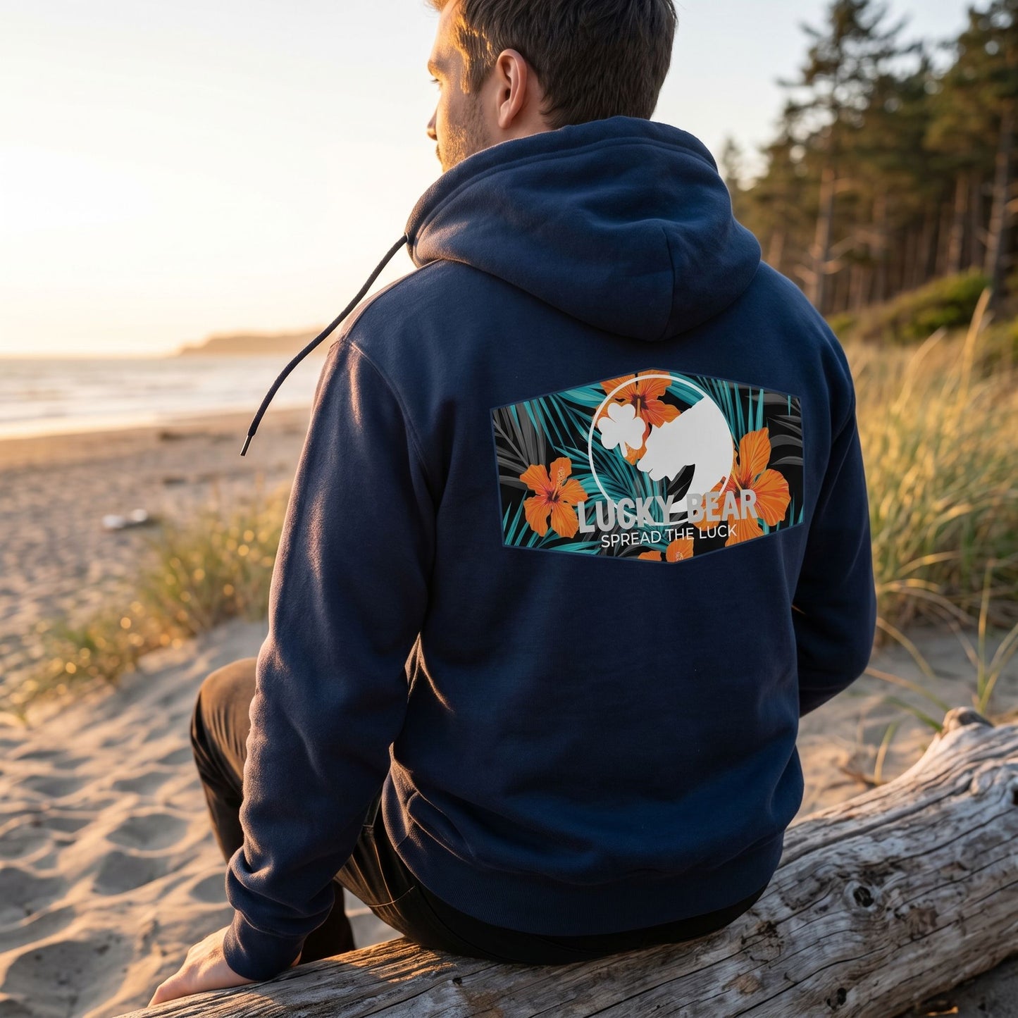 Person sitting on driftwood during golden hour wearing Lucky Bear Tropical Zip Up Hoodie with textured fleece and adjustable drawstrings.