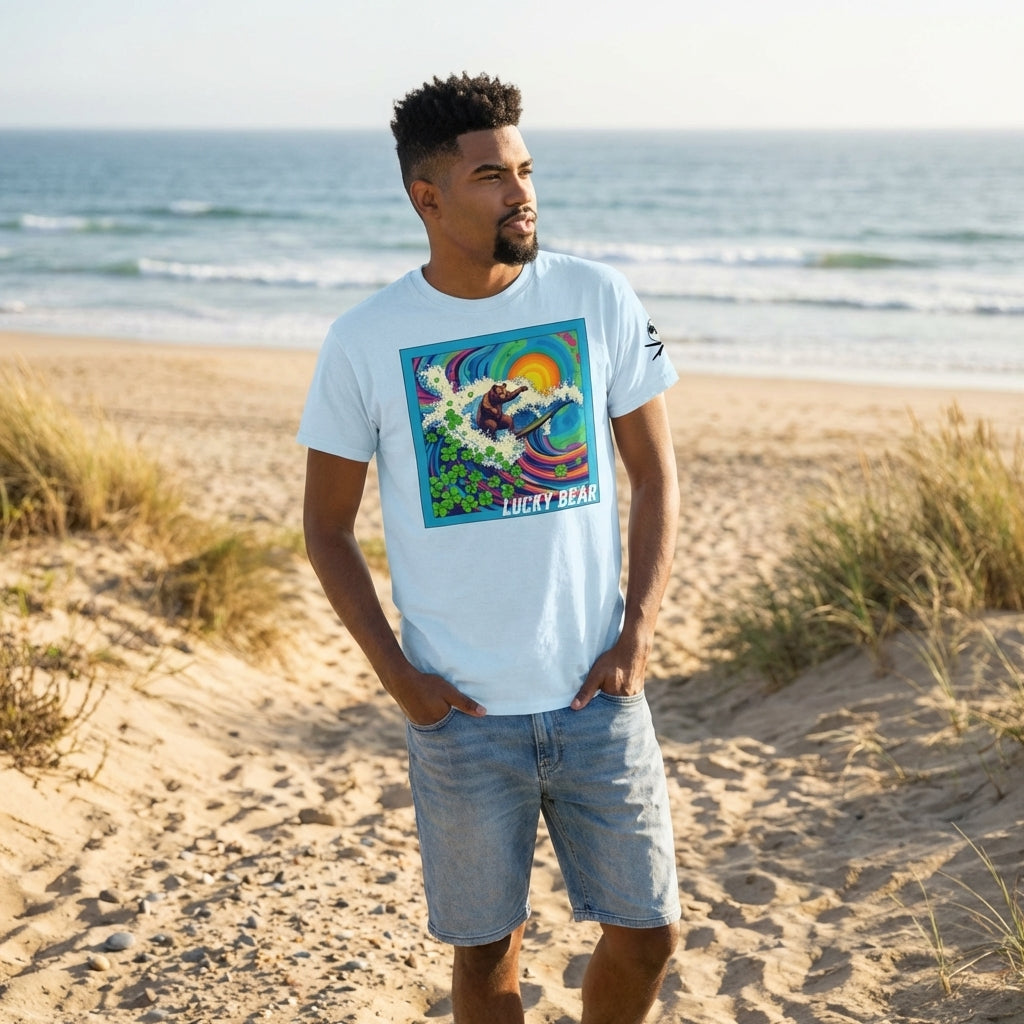 Full-body of a relaxed model wearing Surf Club Riding Waves Tee and light blue shorts on sandy ground by the ocean.