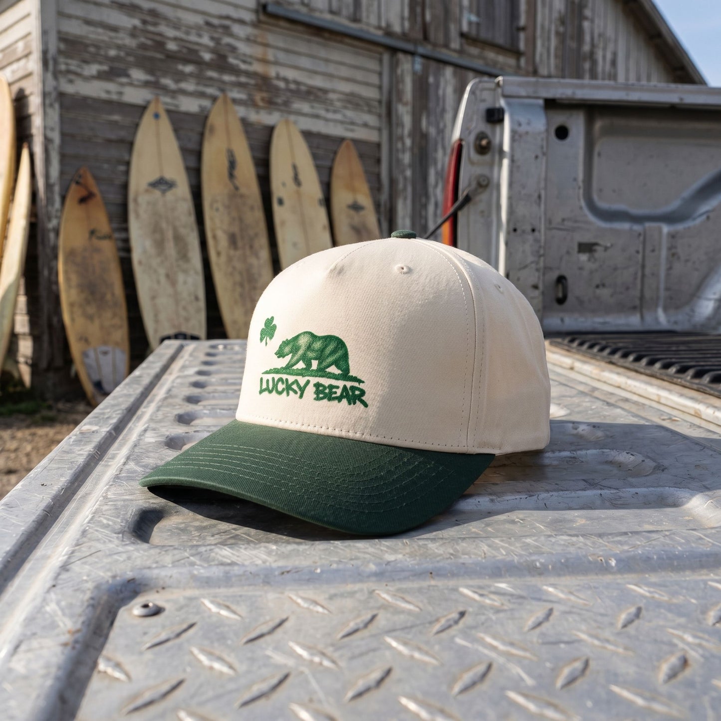 Profile view of Lucky Republic 5 panel cap on truck bed with vintage surfboards, capturing rugged urban-coastal vibe under natural light.