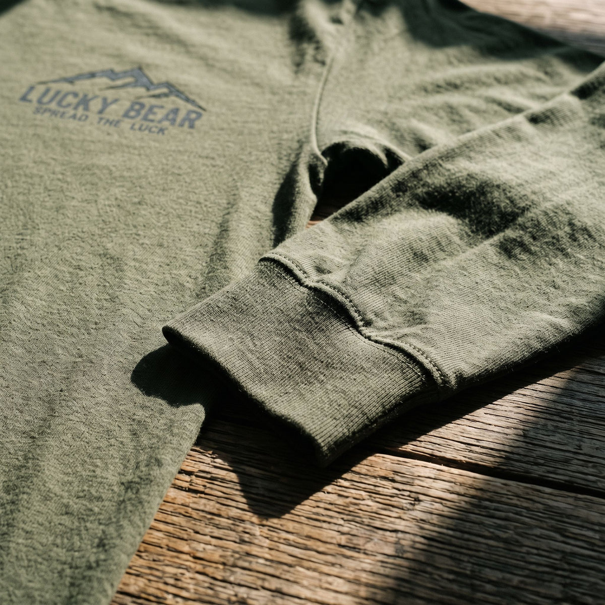 Close-up of Sierra Summit long sleeve shirt fabric weave and cuff stitching on a rustic wooden surface with sunlight shadows.