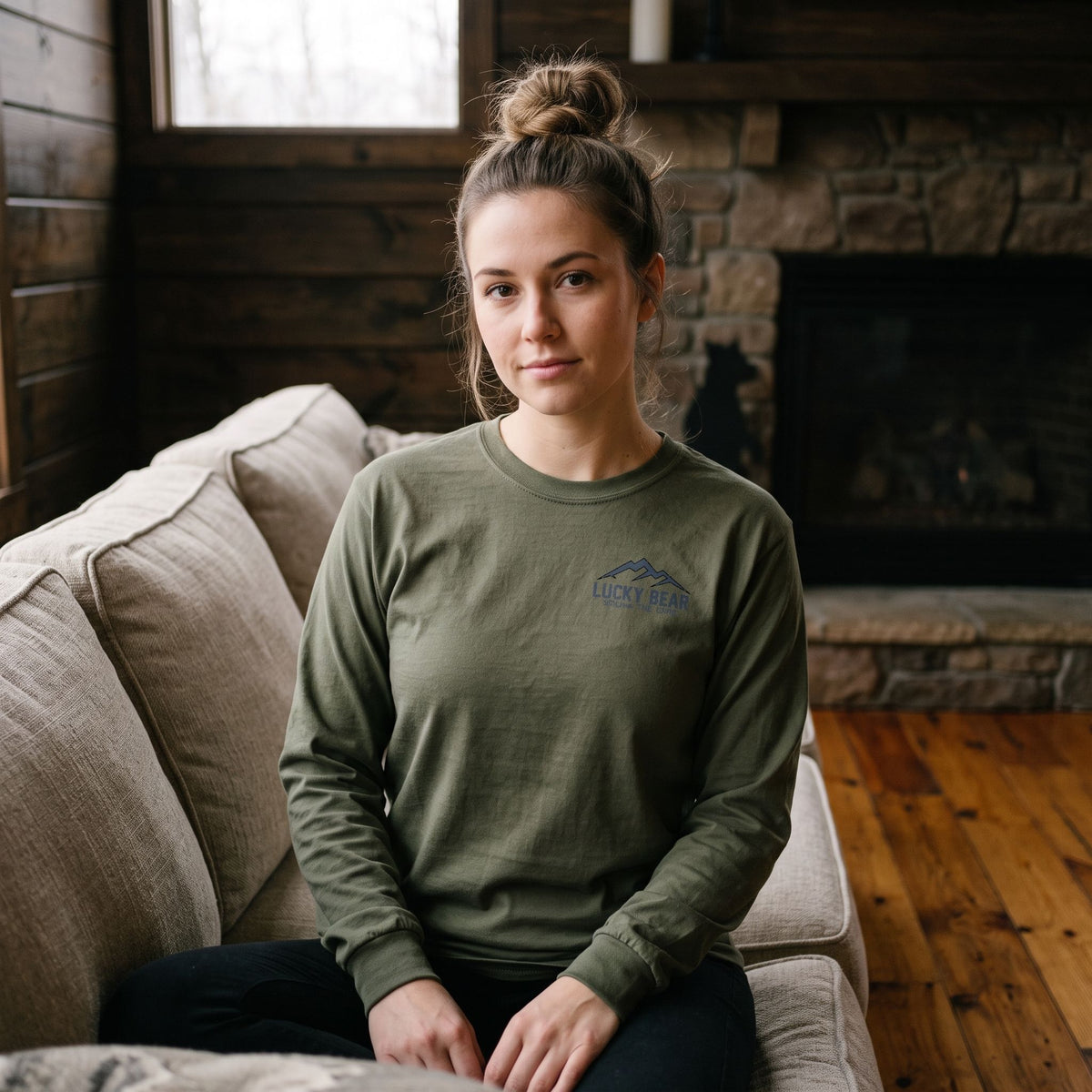 Woman wearing a Sierra Summit long sleeve shirt while sitting on a cozy couch in a rustic mountain cabin.