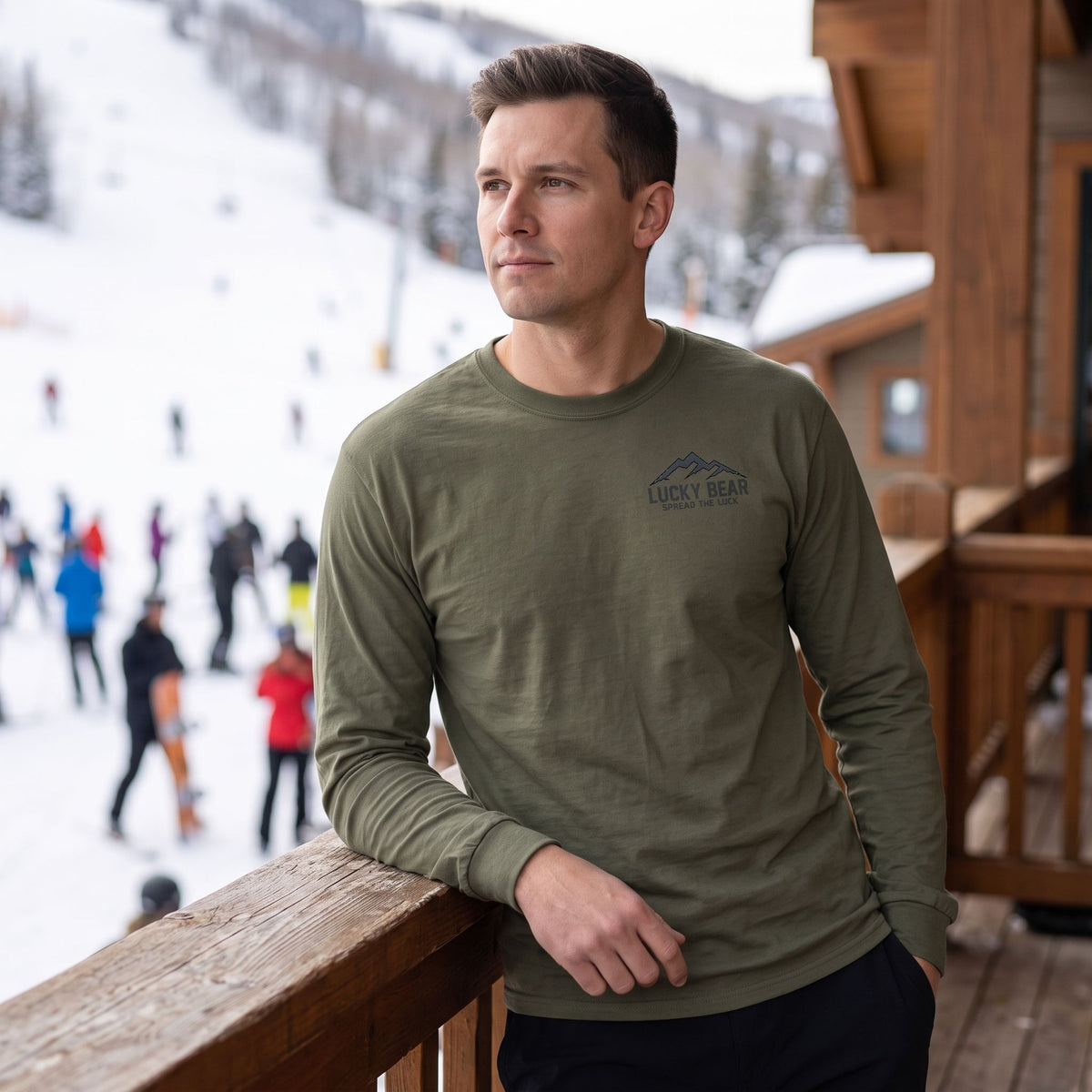 Model wearing a Sierra Summit long sleeve shirt with a small chest logo while leaning on a ski lodge balcony railing.