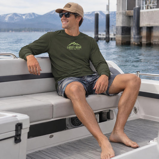 Male model wearing a dark olive Sierra Summit long sleeve shirt with a mountain logo while sitting on a boat at Lake Tahoe.