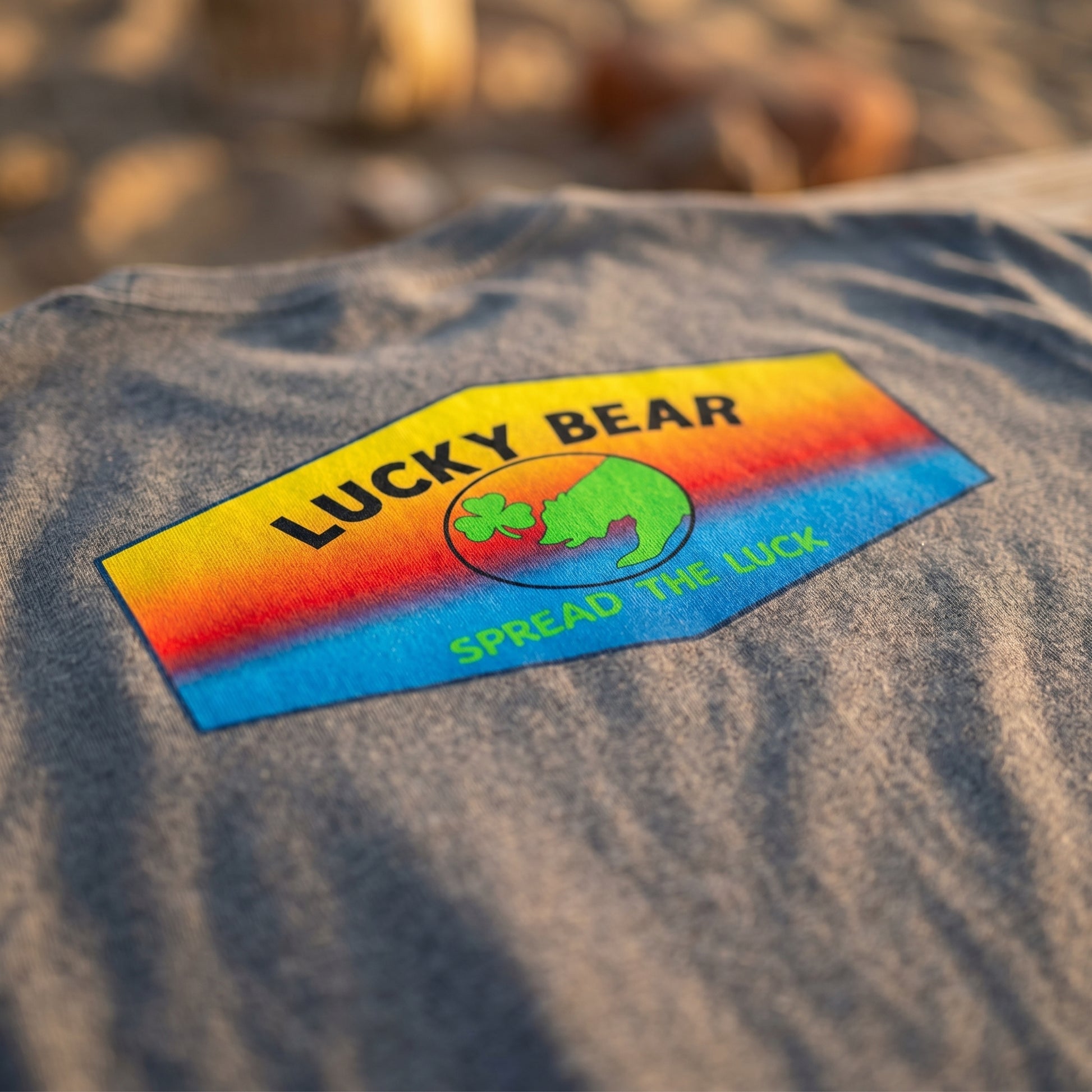 Close-up of the Spread the Luck ombre sunset classic tee fabric showing micro-texture, weave, and sunset hues with natural lighting.