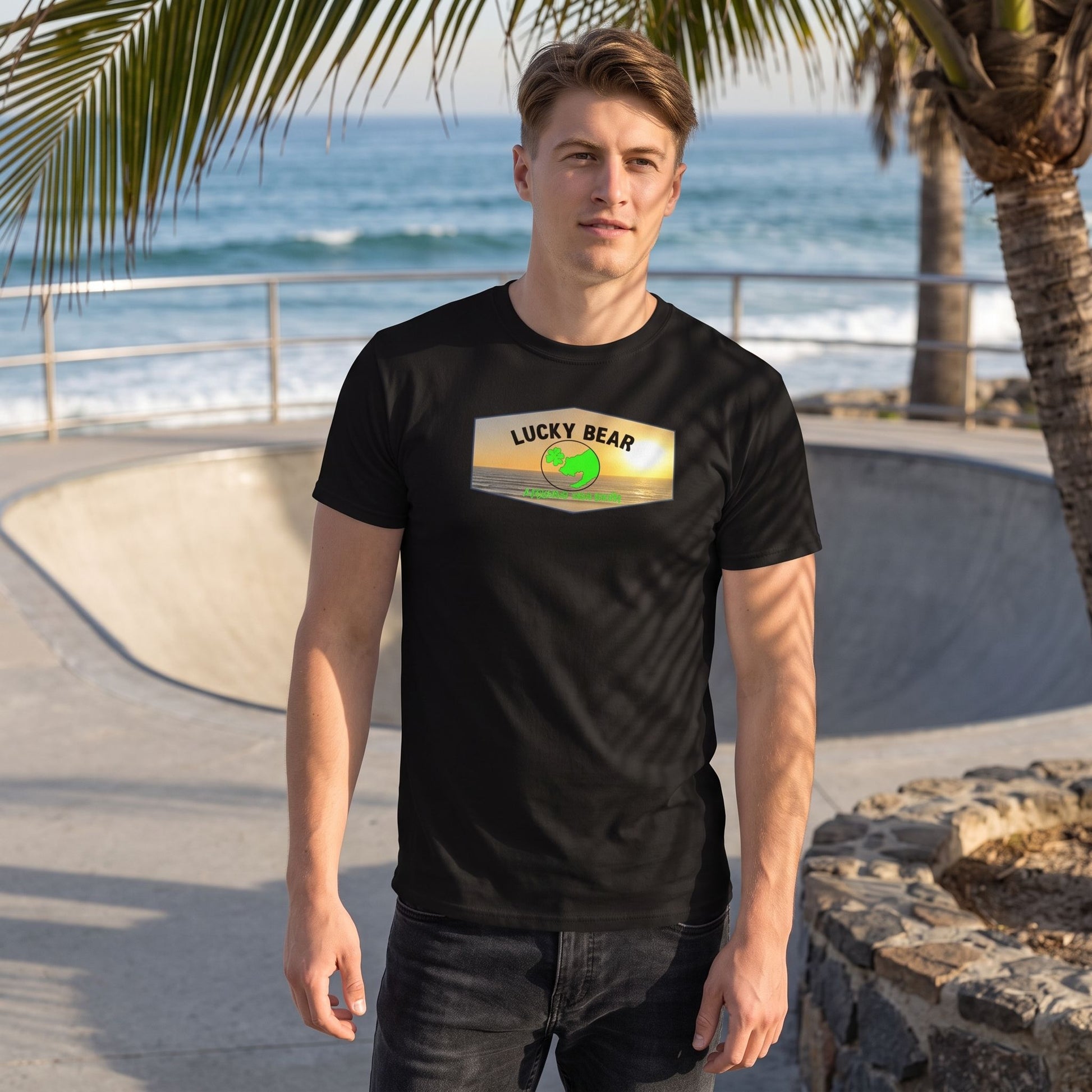Caucasian male wearing Spread the Luck Sunset classic tee in a relaxed pose at a seaside skateboard park with palm trees and natural daylight