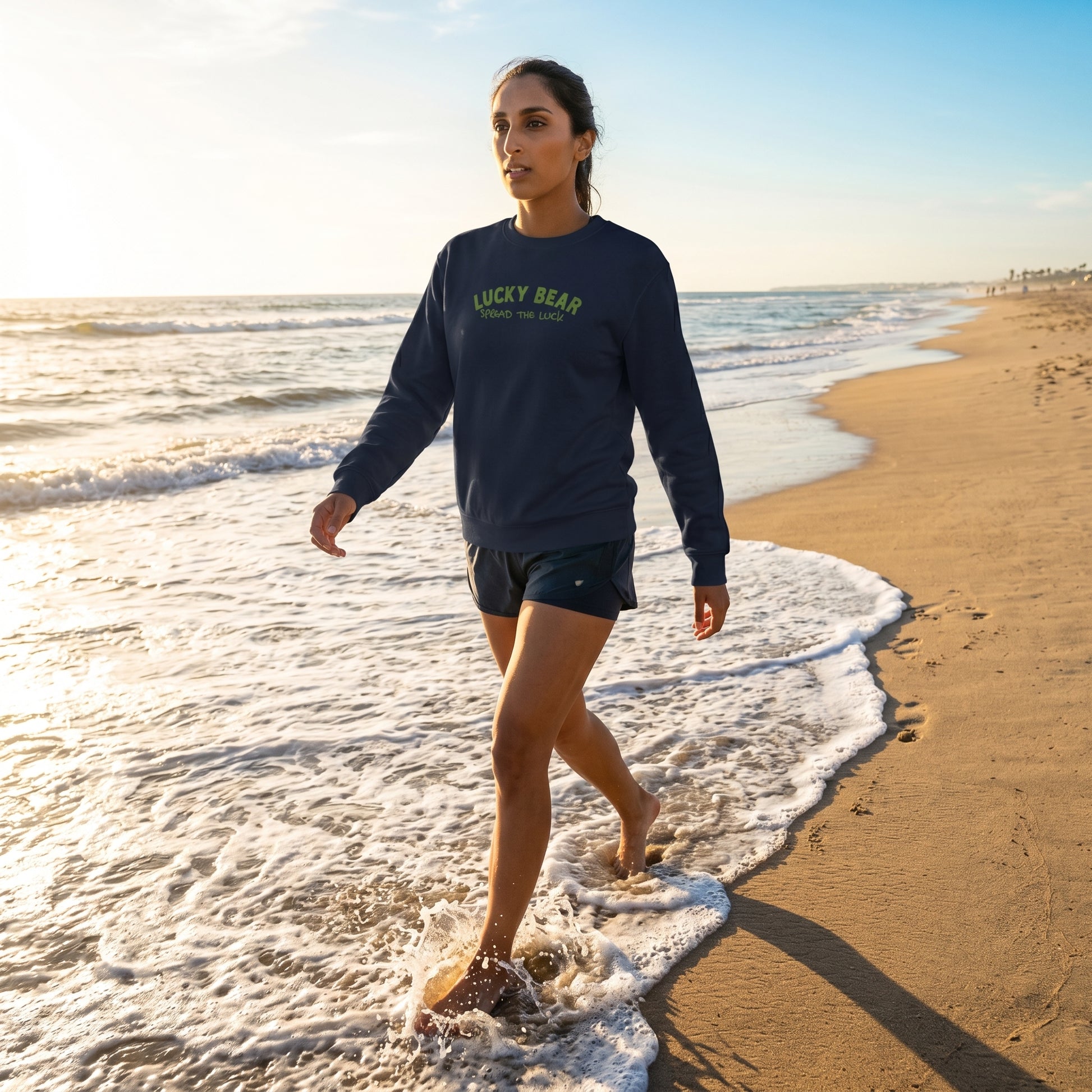 Model wearing Spread the Luck Sweatshirt walking on beach during golden hour, highlighting its fit, texture, and comfort with natural lighting.