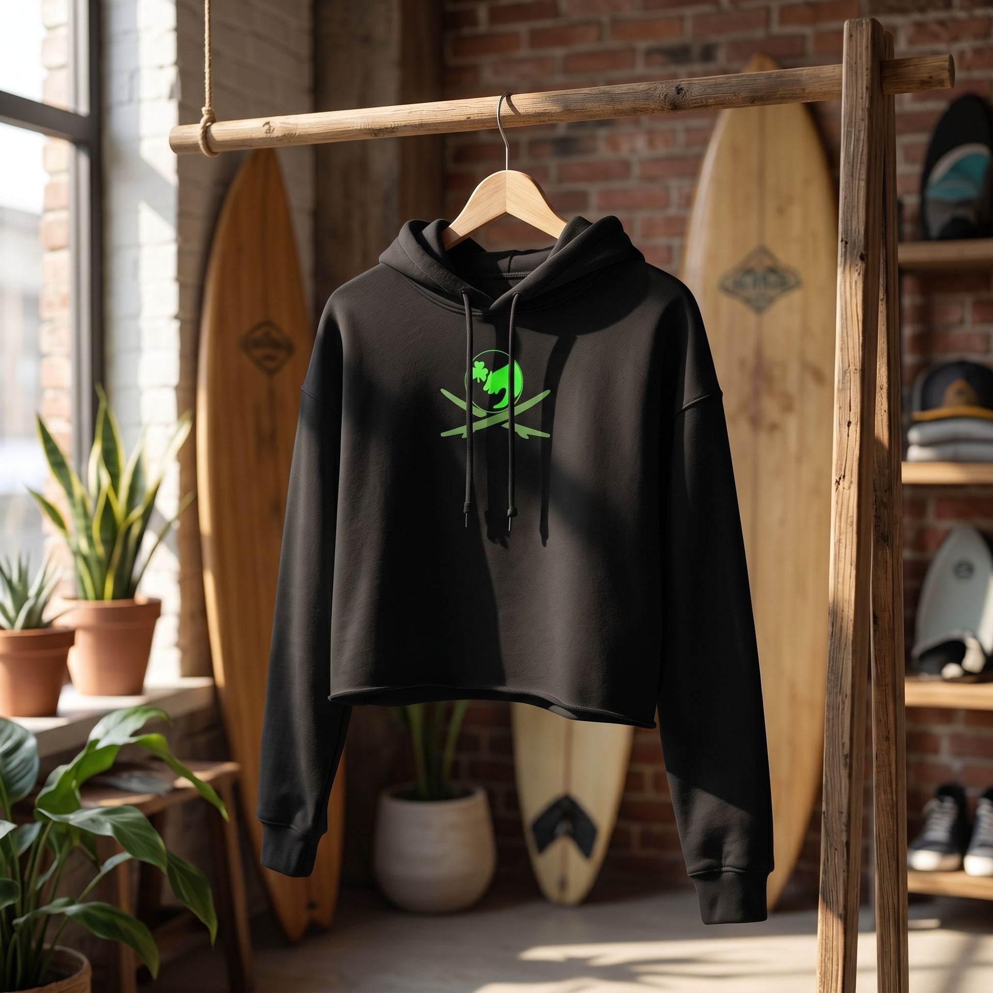 Surf Club Logo Crop Hoodie hanging on a rustic wooden rack in a surf boutique, styled with coastal decor and natural light.