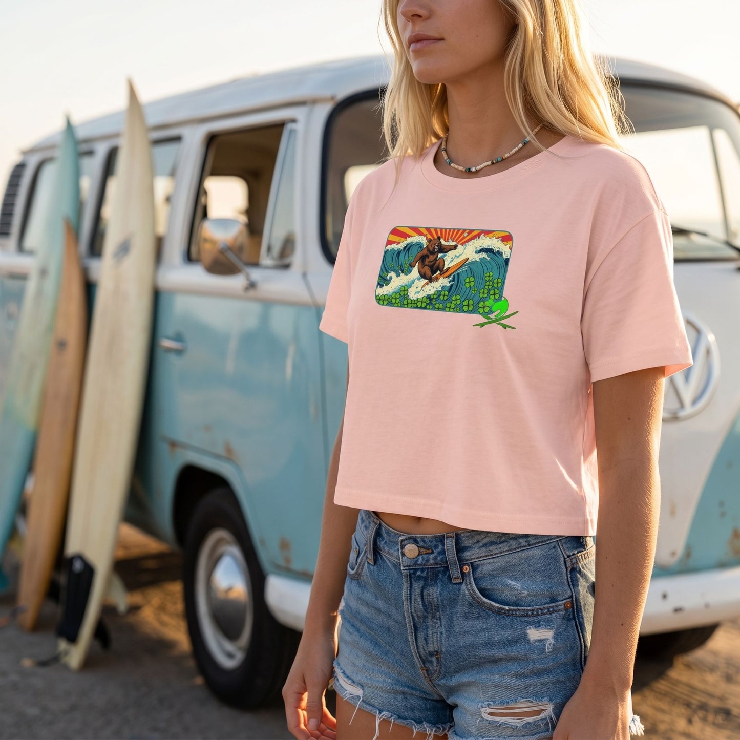 Model wearing crop top with jean shorts near vintage VW van with surfboards, sunlit scene highlighting fabric micro-texture.