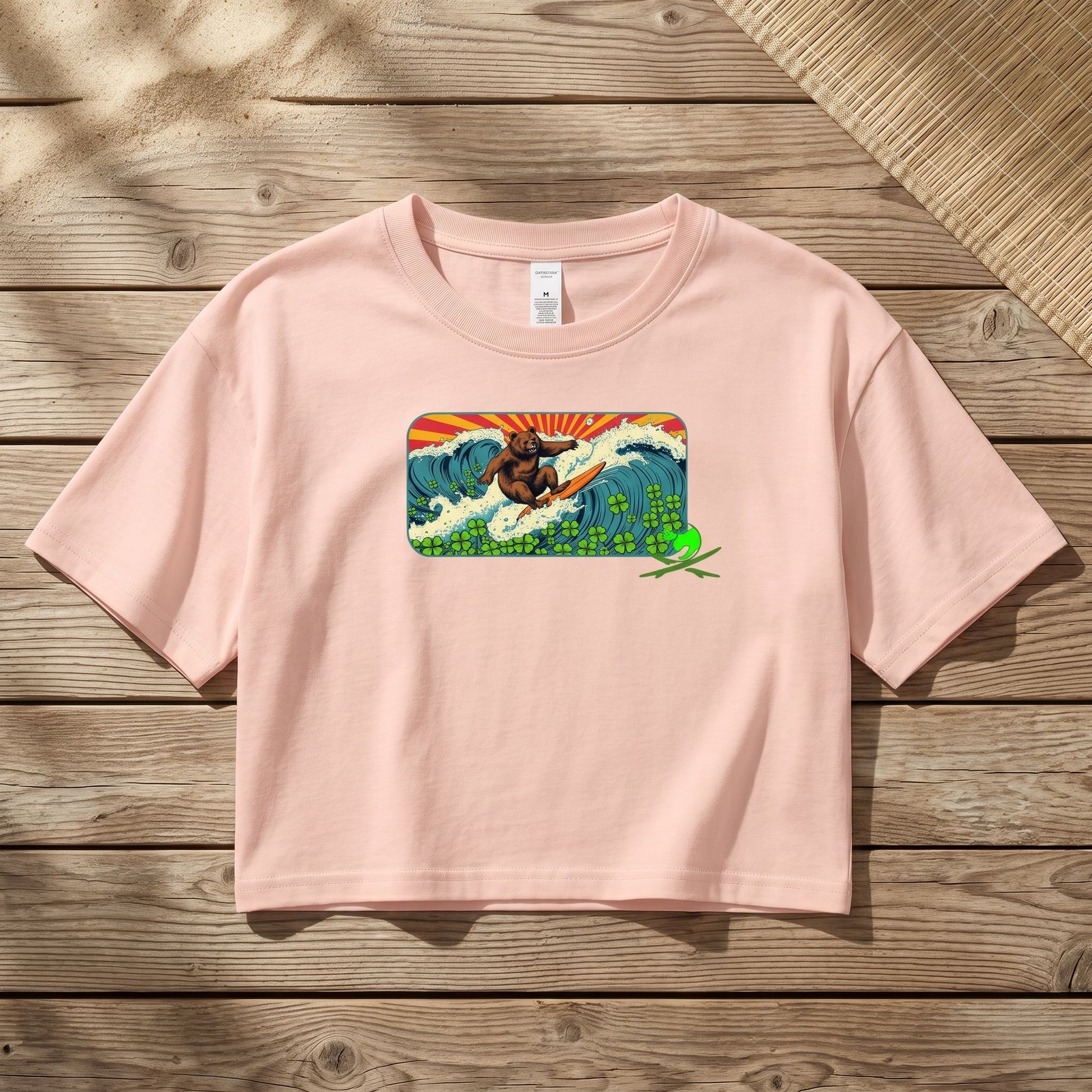 Surf Club Retro Bear women's crop top displayed on textured wooden surface with natural daylight, highlighting vibrant pink color and fabric details.