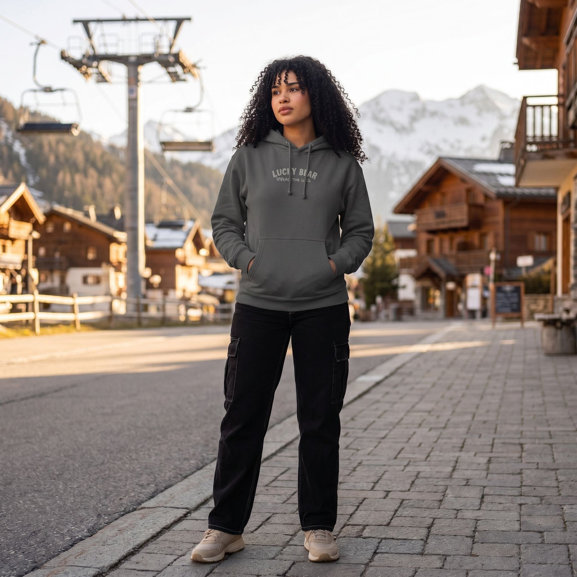 Casually posed model wearing Spread the Luck heavyweight hoodie outdoors during golden hour, highlighting textured fabric and relaxed fit with mountain resort backdrop.