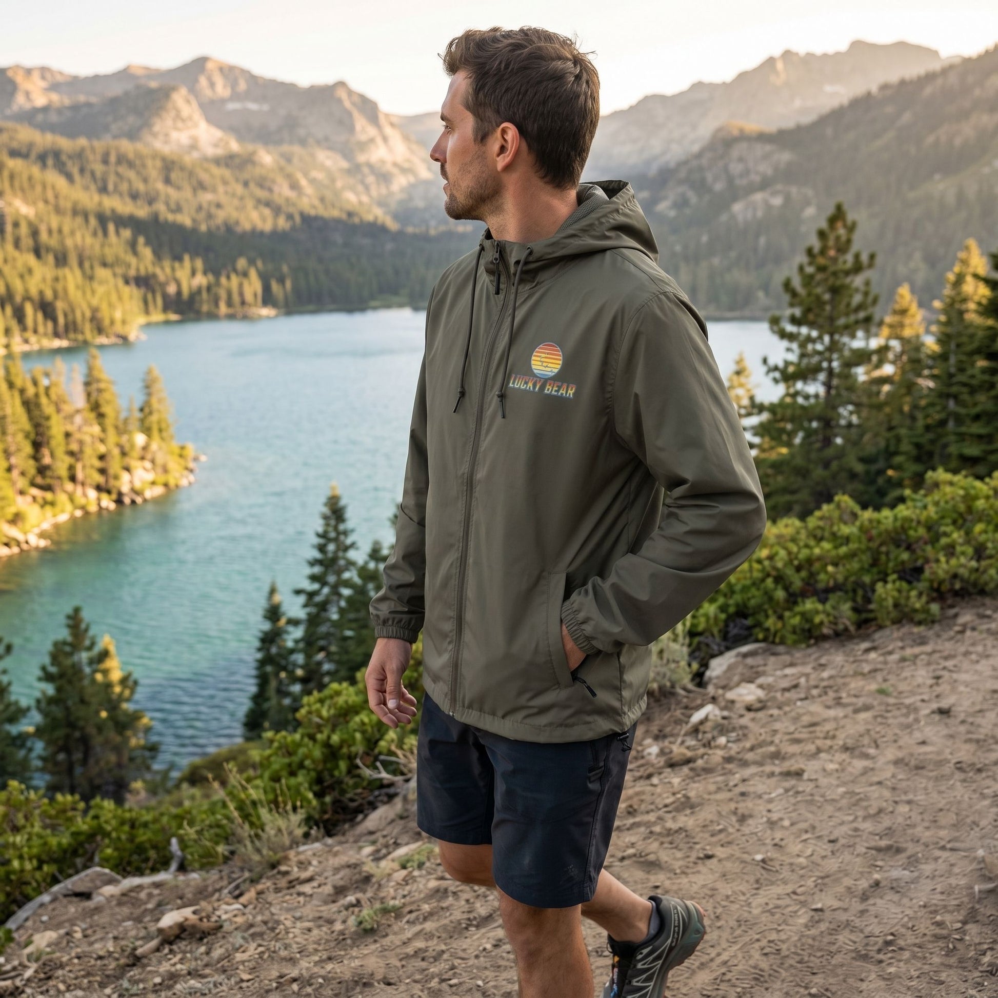 Unisex retro sunset windbreaker worn by model on trail overlooking Lake Tahoe during golden hour, highlighting water-resistant fabric and practical features.