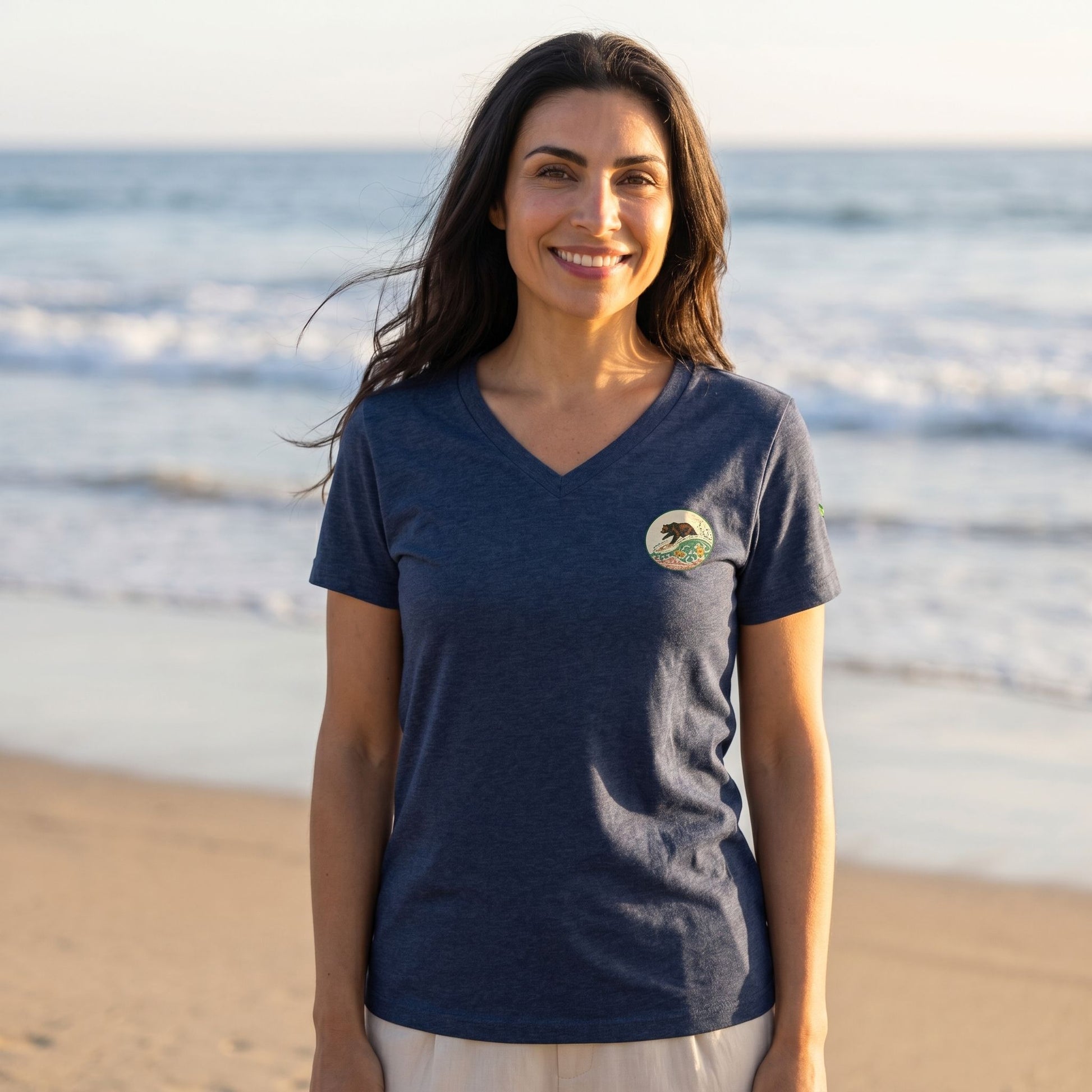 Relaxed female model wearing women's Surf Club vintage v-neck t-shirt on a sandy beach during golden hour sunlight.