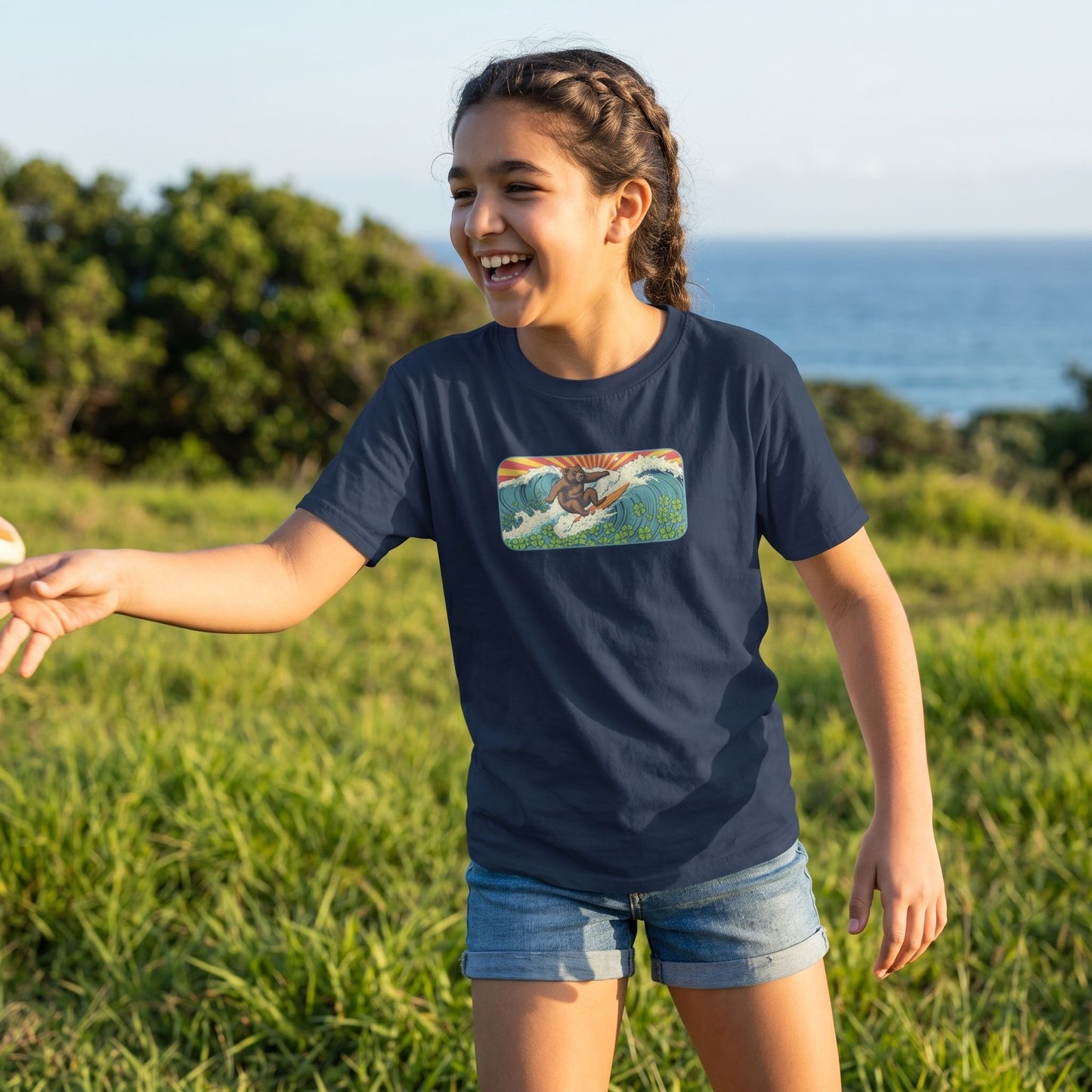 Young girl in Surf Club Retro Bear Youth Tee playing outdoors during golden hour with lush greenery and ocean hints, showcasing the comfortable cotton fabric.